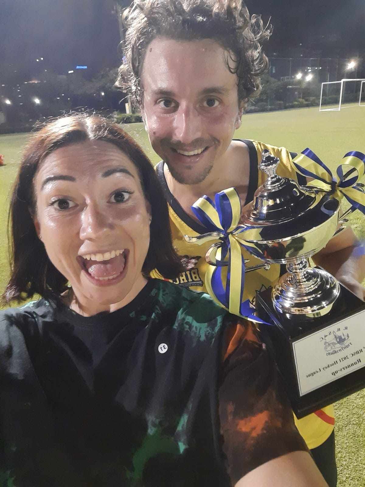 A man and a woman are posing for a picture while holding a trophy.