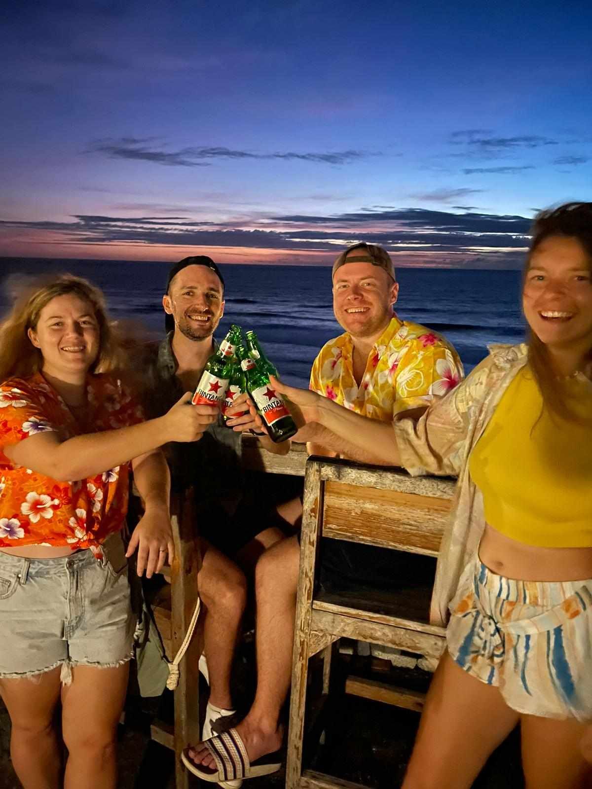 A group of people are sitting on a beach holding bottles of beer.
