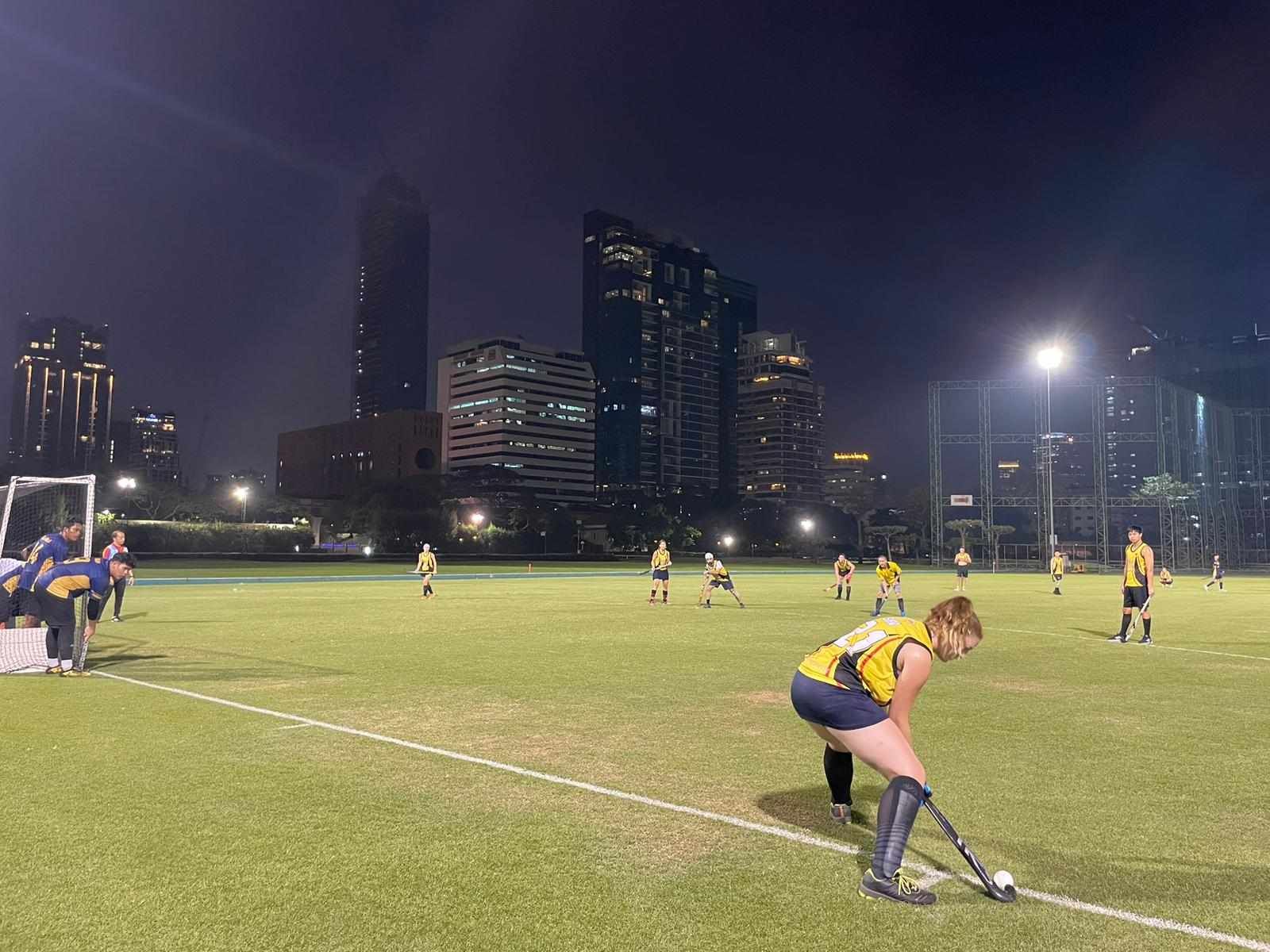 A group of people are playing field hockey on a field at night.