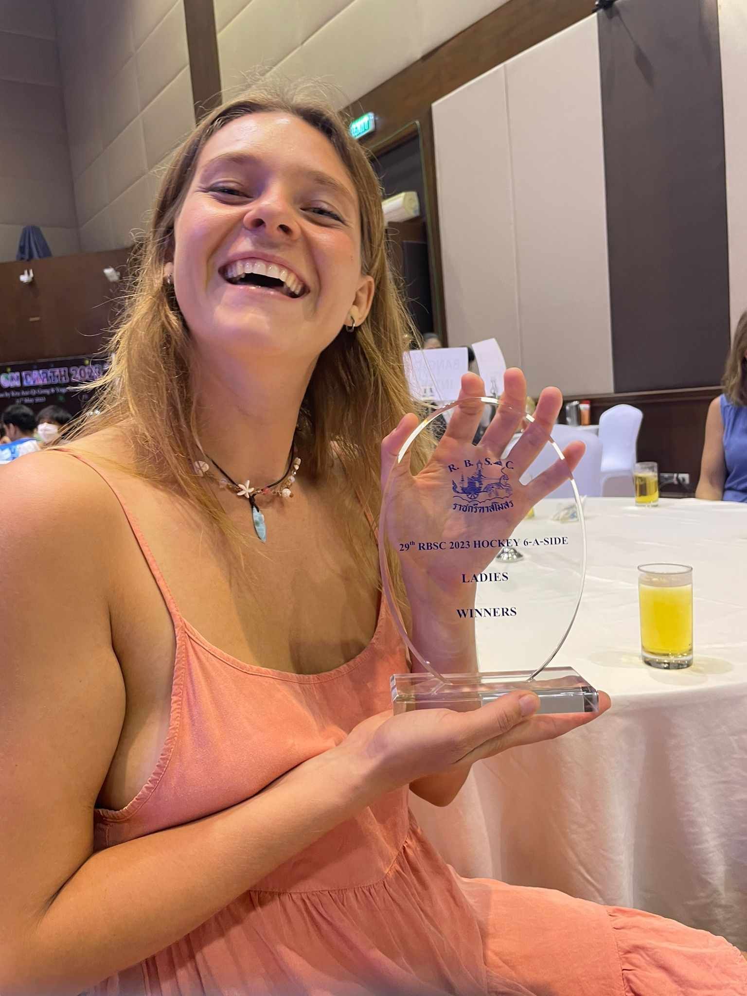 A woman in a pink dress is holding a trophy and smiling.