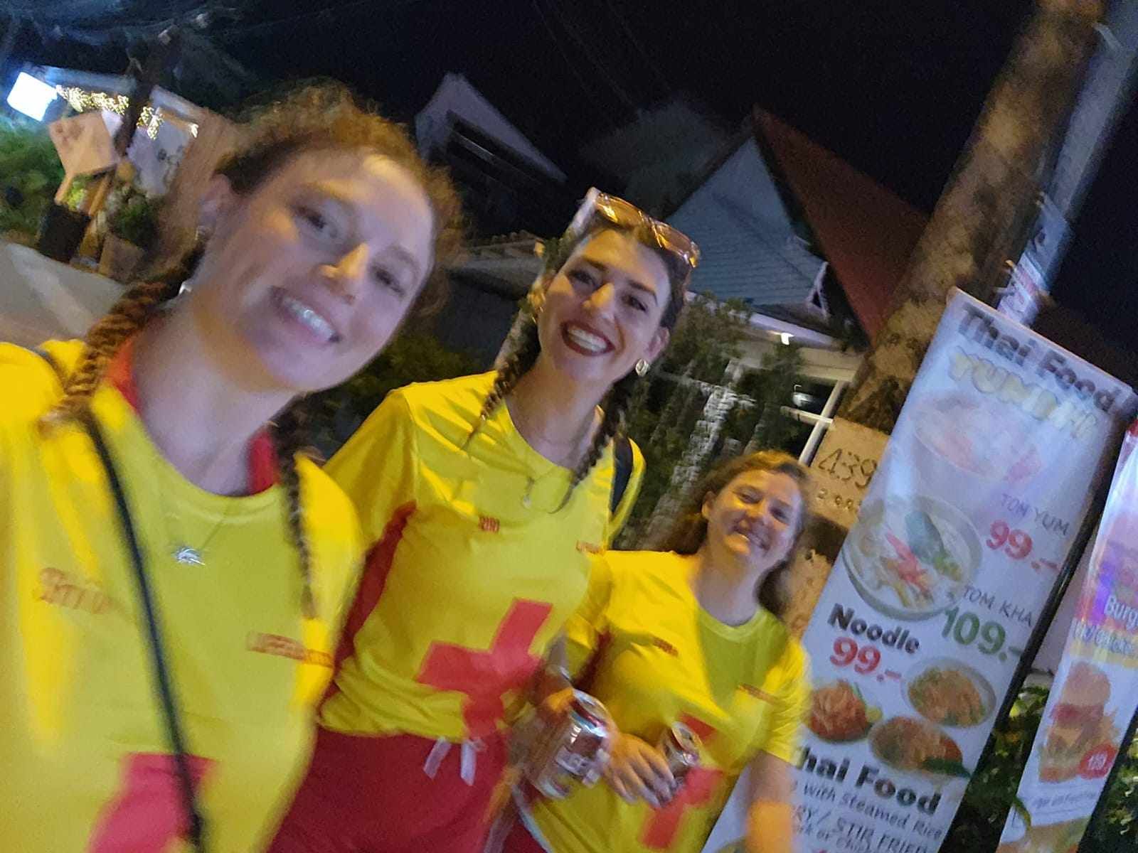 Three women wearing yellow shirts with a red cross on them are posing for a picture.