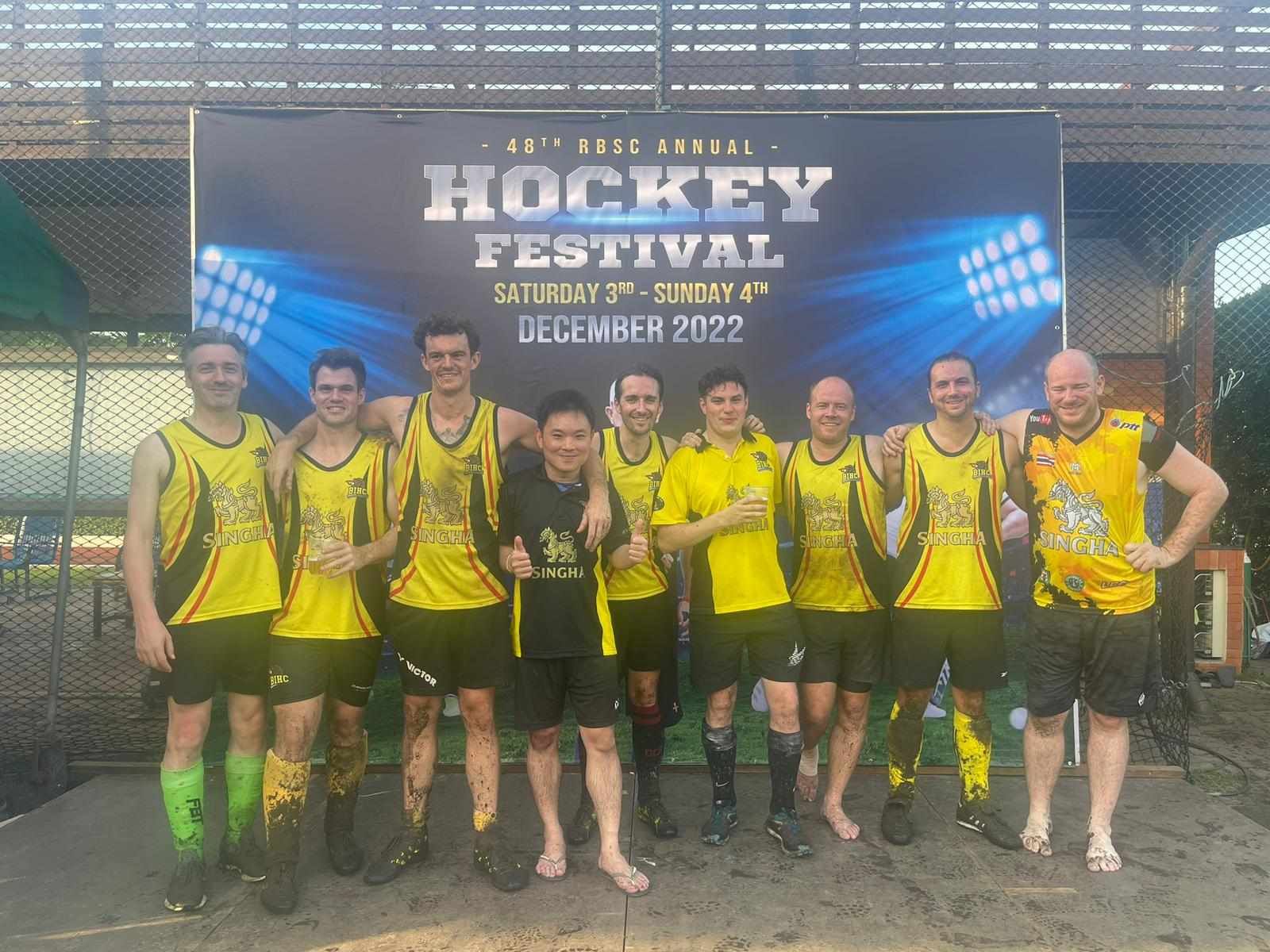 A group of men are posing for a picture in front of a hockey festival sign.
