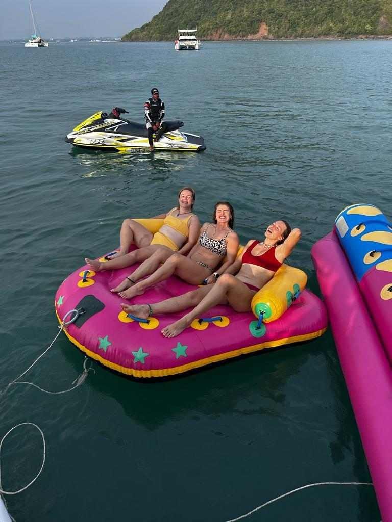 Three women are sitting on a pink raft in the water.