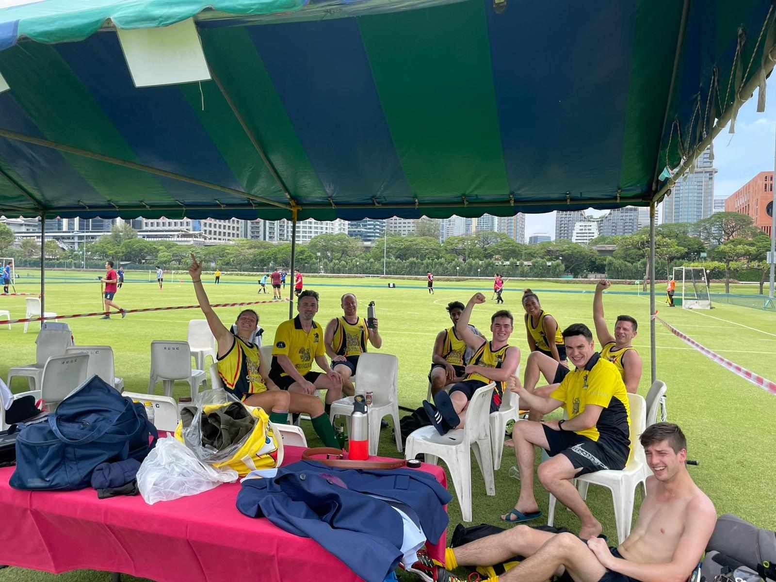 A group of people are sitting under a tent on a field.
