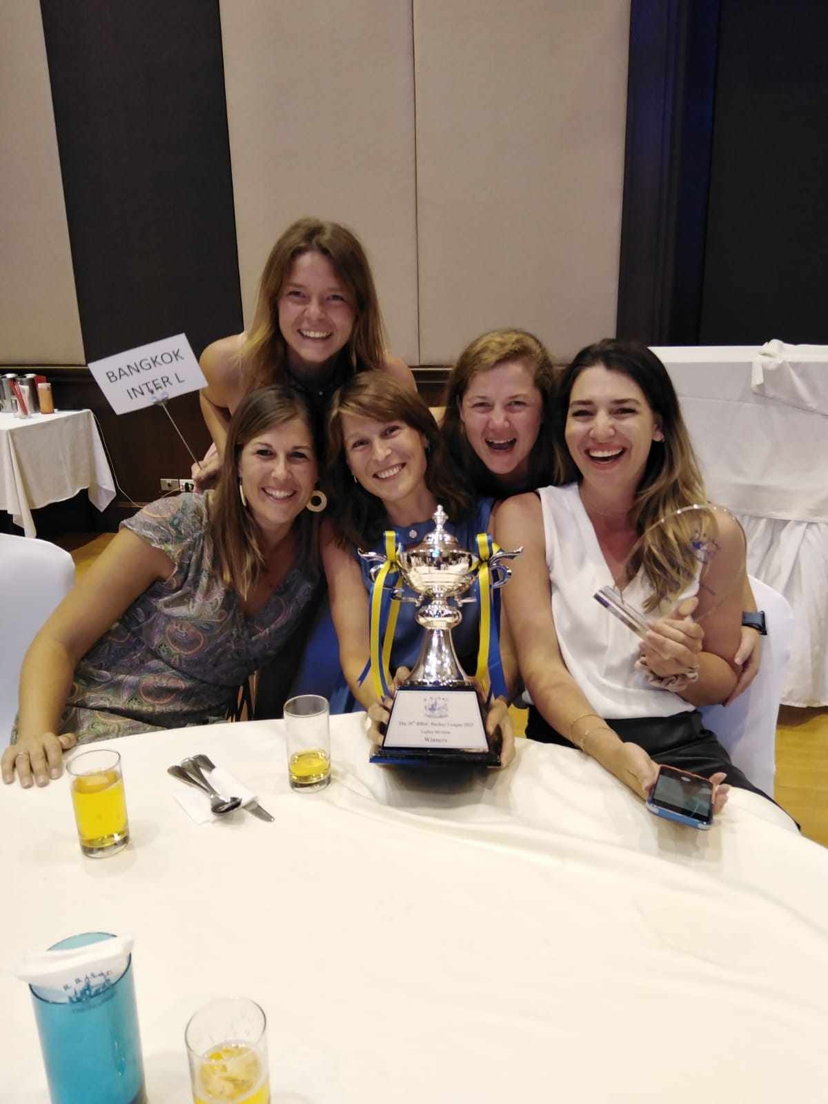 A group of women are sitting around a table holding a trophy.