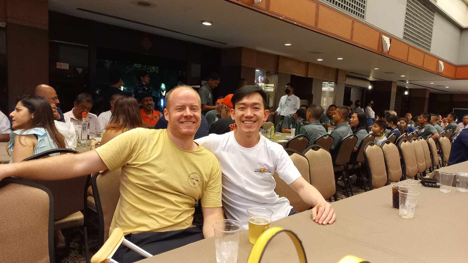 Two men are posing for a picture while sitting at a table in a restaurant.