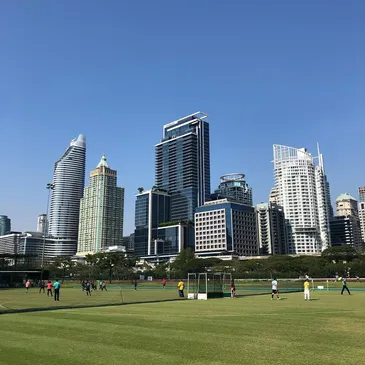 A group of people are playing soccer in a field in front of a city skyline.