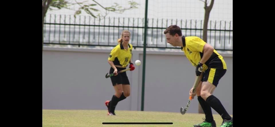 A man and a woman are playing field hockey on a field.