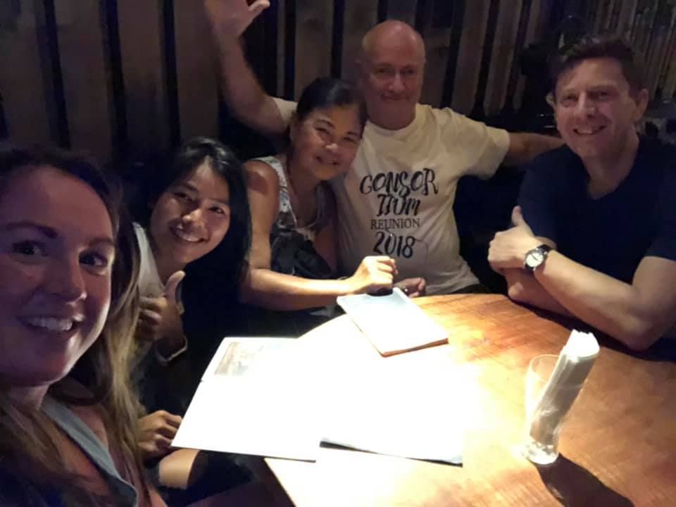 A group of people are sitting around a table with a man wearing a concert mon shirt