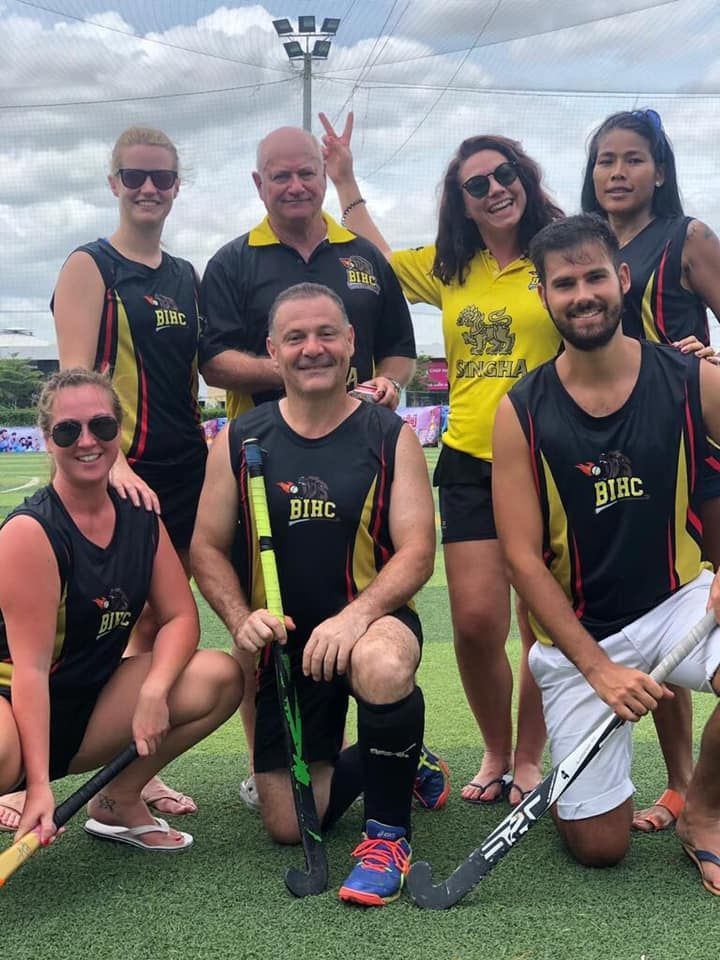A group of people are posing for a picture on a field with hockey sticks.