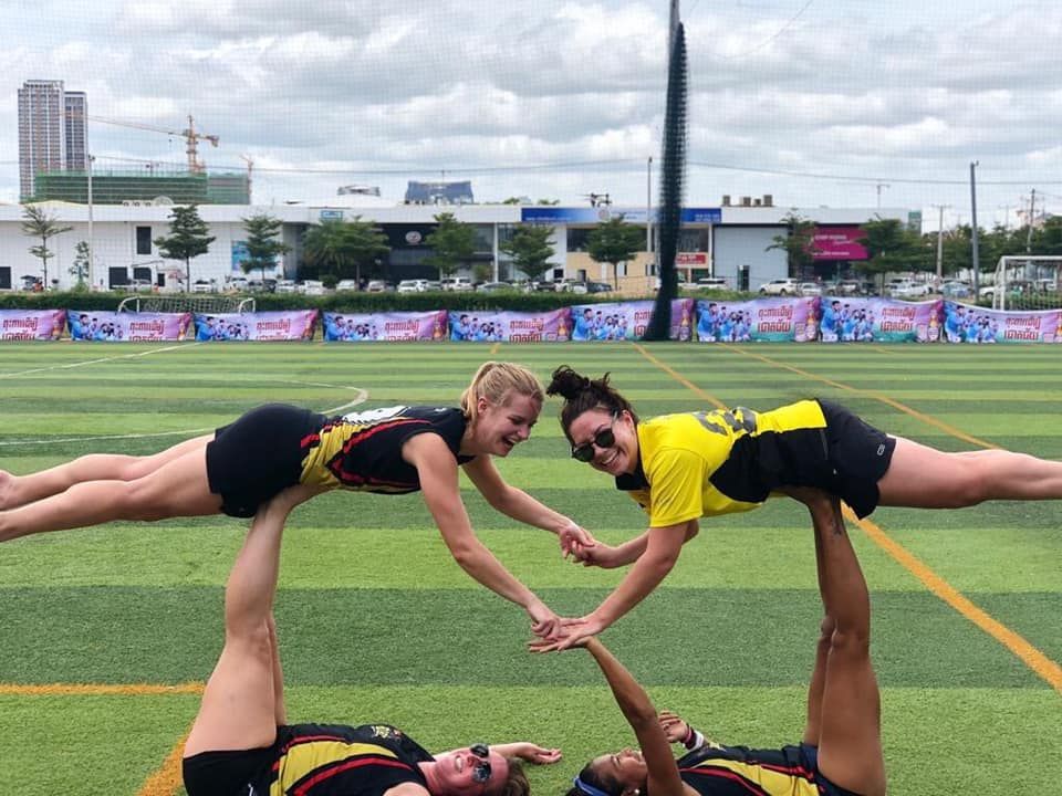 Three cheerleaders are doing a handstand on a field.