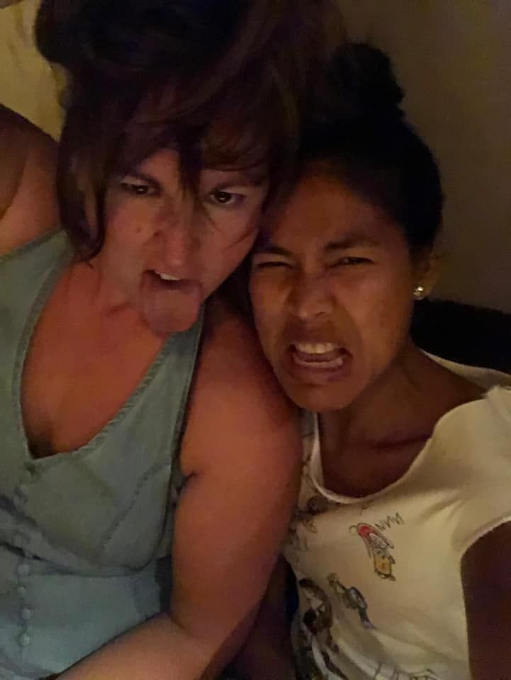 Two women are making funny faces while sitting next to each other on a bed.
