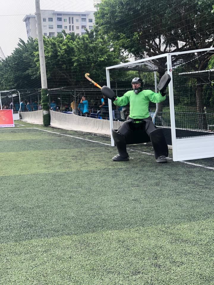 A man in a green uniform is holding a hockey stick on a field.
