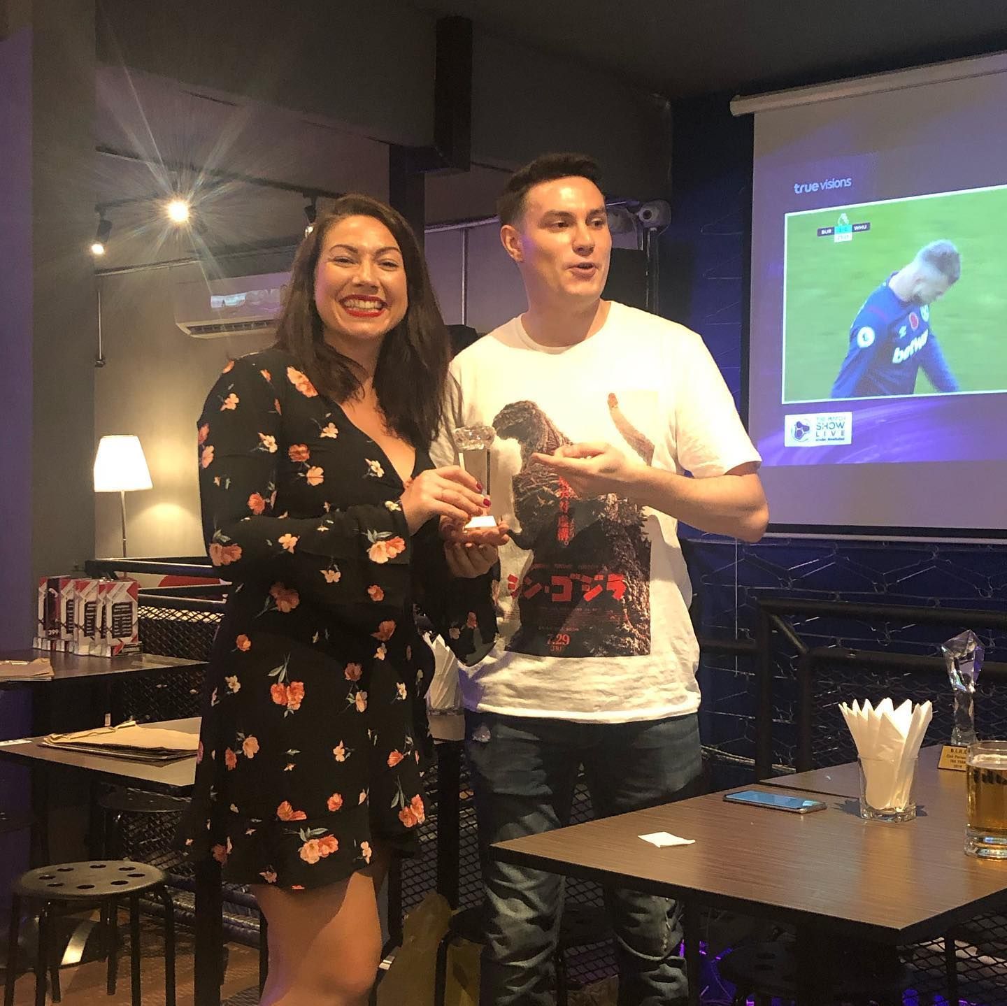 A man and a woman are standing in front of a projector screen in a restaurant.