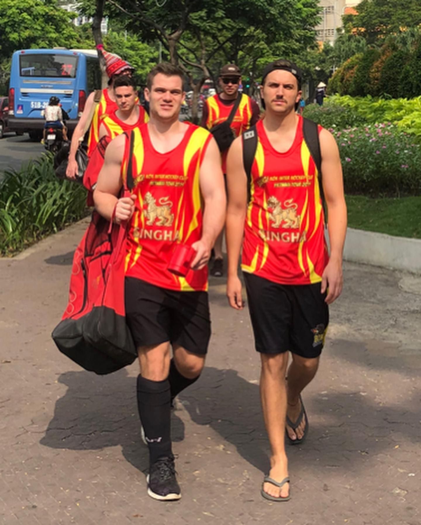A group of men are walking down a street wearing singha jerseys