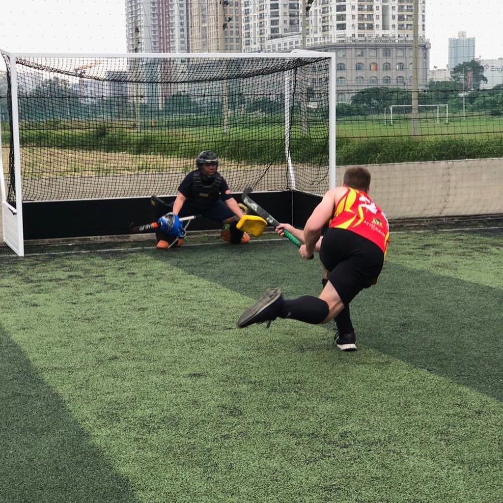 A man is playing field hockey on a field with a goalie in the background.