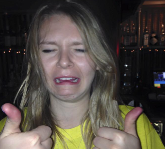 A woman in a yellow shirt is crying and giving a thumbs up
