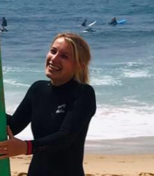 A woman in a wetsuit is holding a surfboard on the beach.