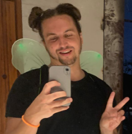 A man wearing fairy wings is taking a selfie with his phone