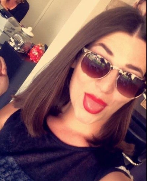 A woman wearing sunglasses and red lipstick is taking a selfie