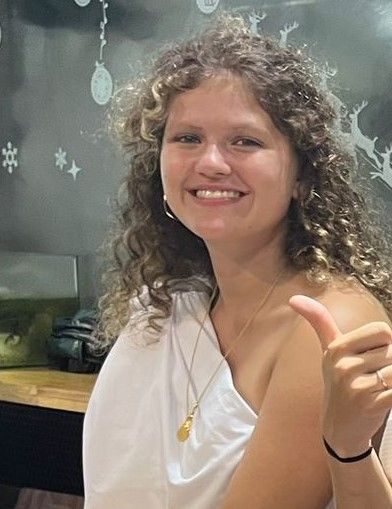 A woman with curly hair is smiling and giving a thumbs up.