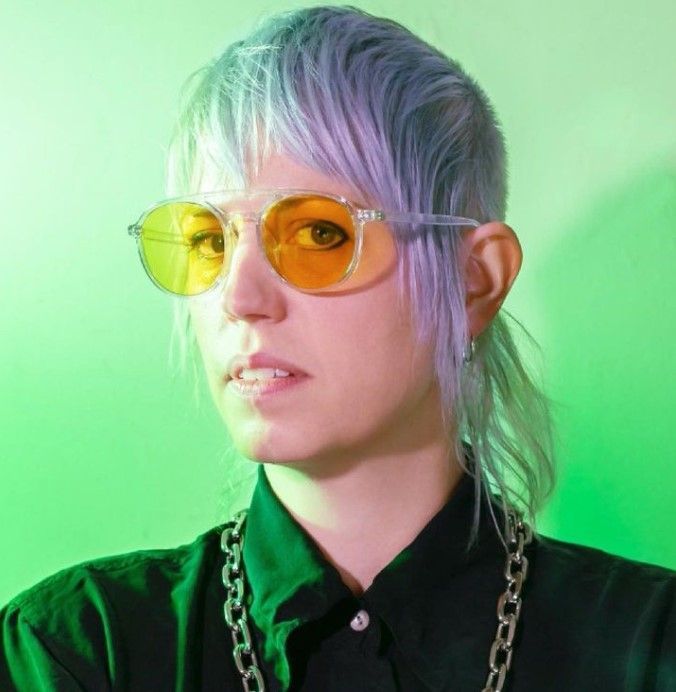 A woman with purple hair is wearing sunglasses and a chain around her neck.