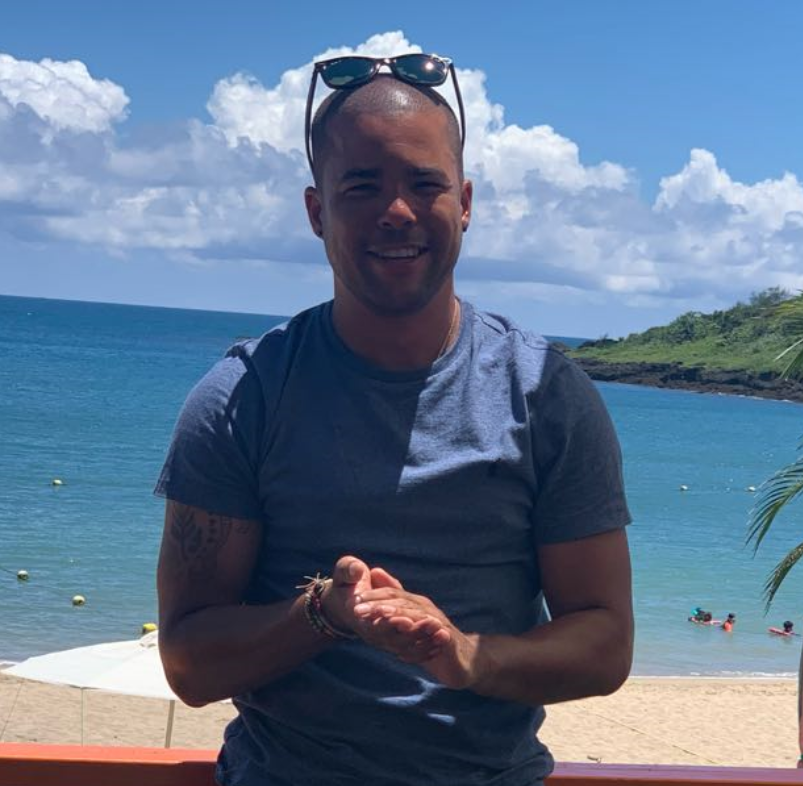 A man wearing sunglasses stands in front of the ocean