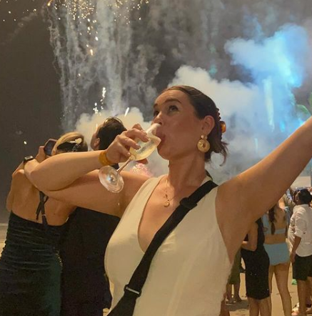 A woman is drinking a glass of champagne in front of fireworks