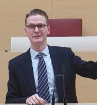 A man in a suit and tie is standing at a podium.