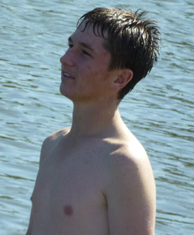 Young man in water, shirtless, looking up with a slight smile.