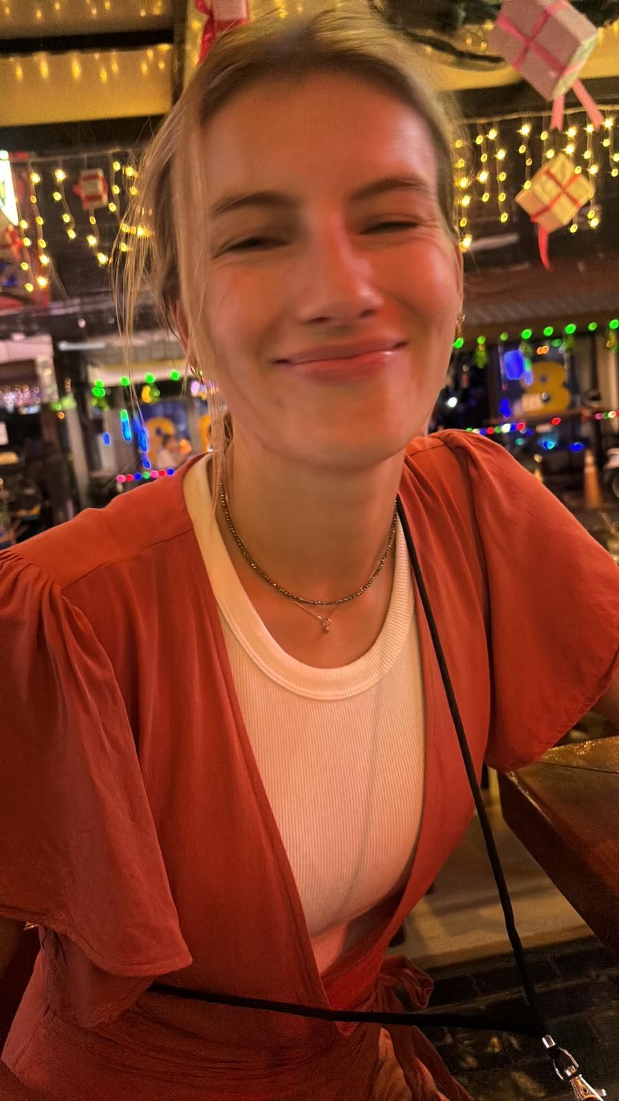 A woman in a red dress is smiling while sitting at a bar.