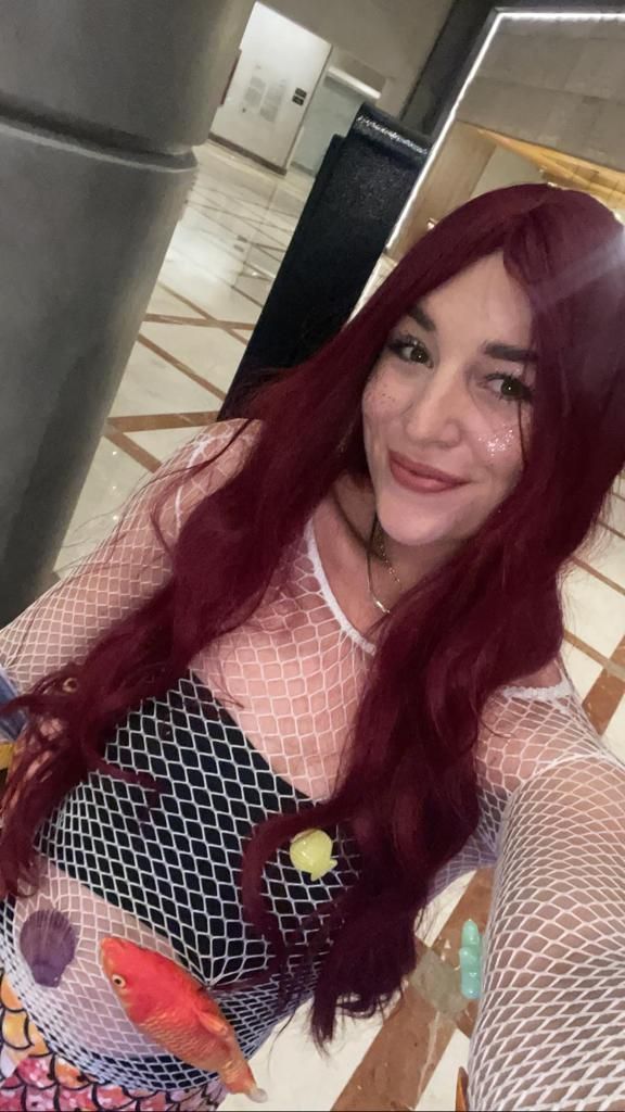 A woman with long red hair is taking a selfie in front of a mirror.