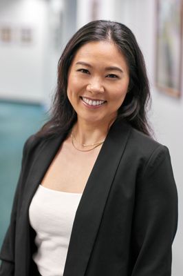 A woman in a black jacket and white top is smiling for the camera.