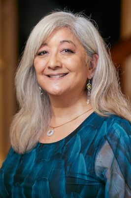A woman with gray hair and a blue shirt is smiling for the camera.