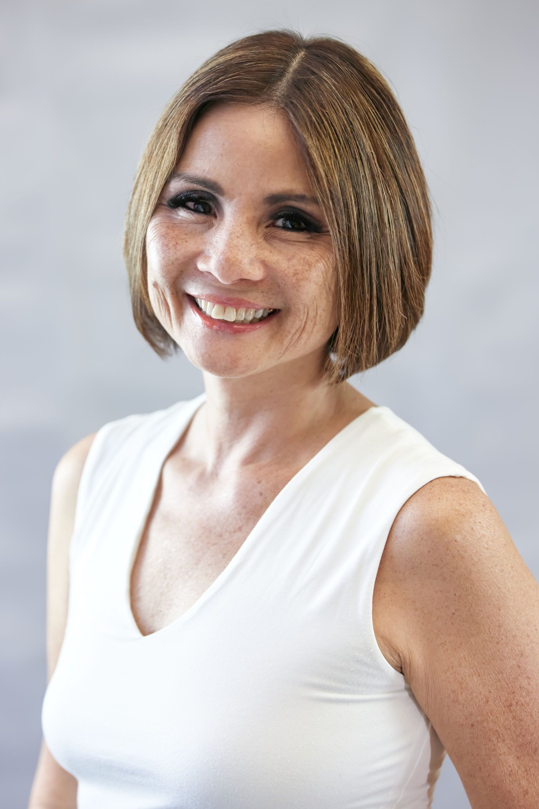A woman in a white tank top is smiling for the camera.