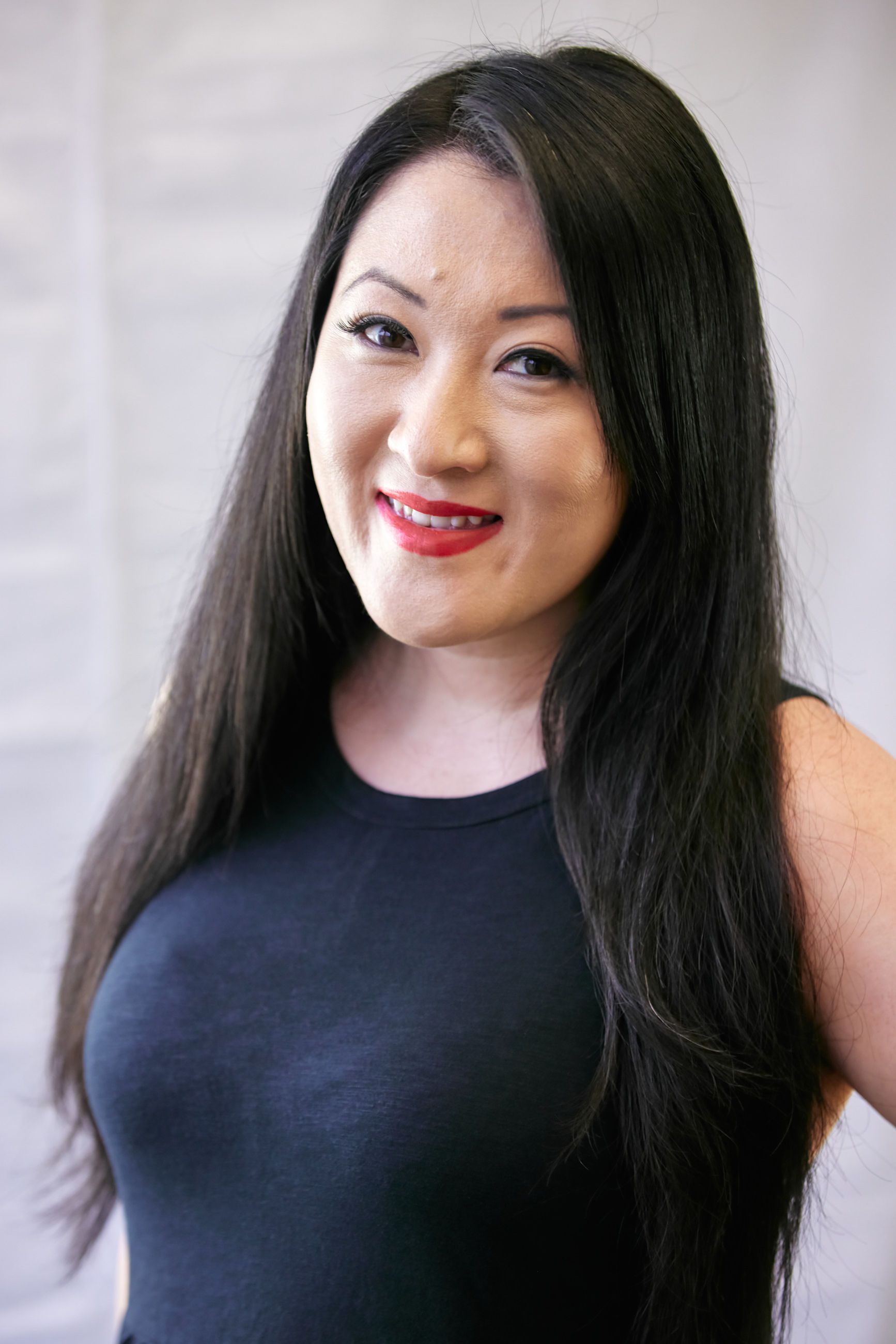 A woman with long black hair is wearing a black tank top and red lipstick.