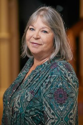 A woman with gray hair and blue eyes is smiling for the camera.