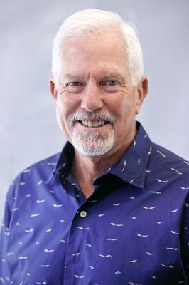 A man with a beard and a blue shirt is smiling for the camera.