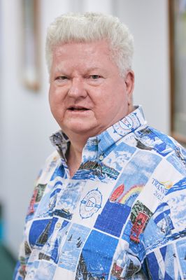 A man with white hair is wearing a blue and white shirt.
