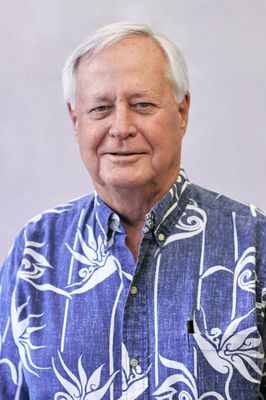 A man wearing a blue and white hawaiian shirt is smiling for the camera.