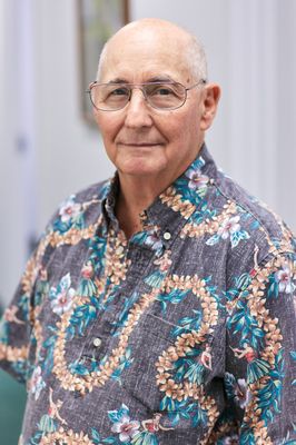 A bald man wearing glasses and a floral shirt is standing in a room.