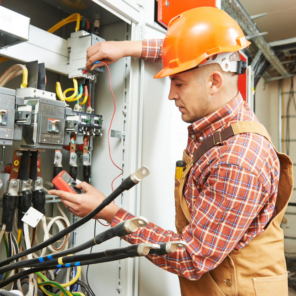 Electrician in orange hard hat, testing wires in an electrical panel.