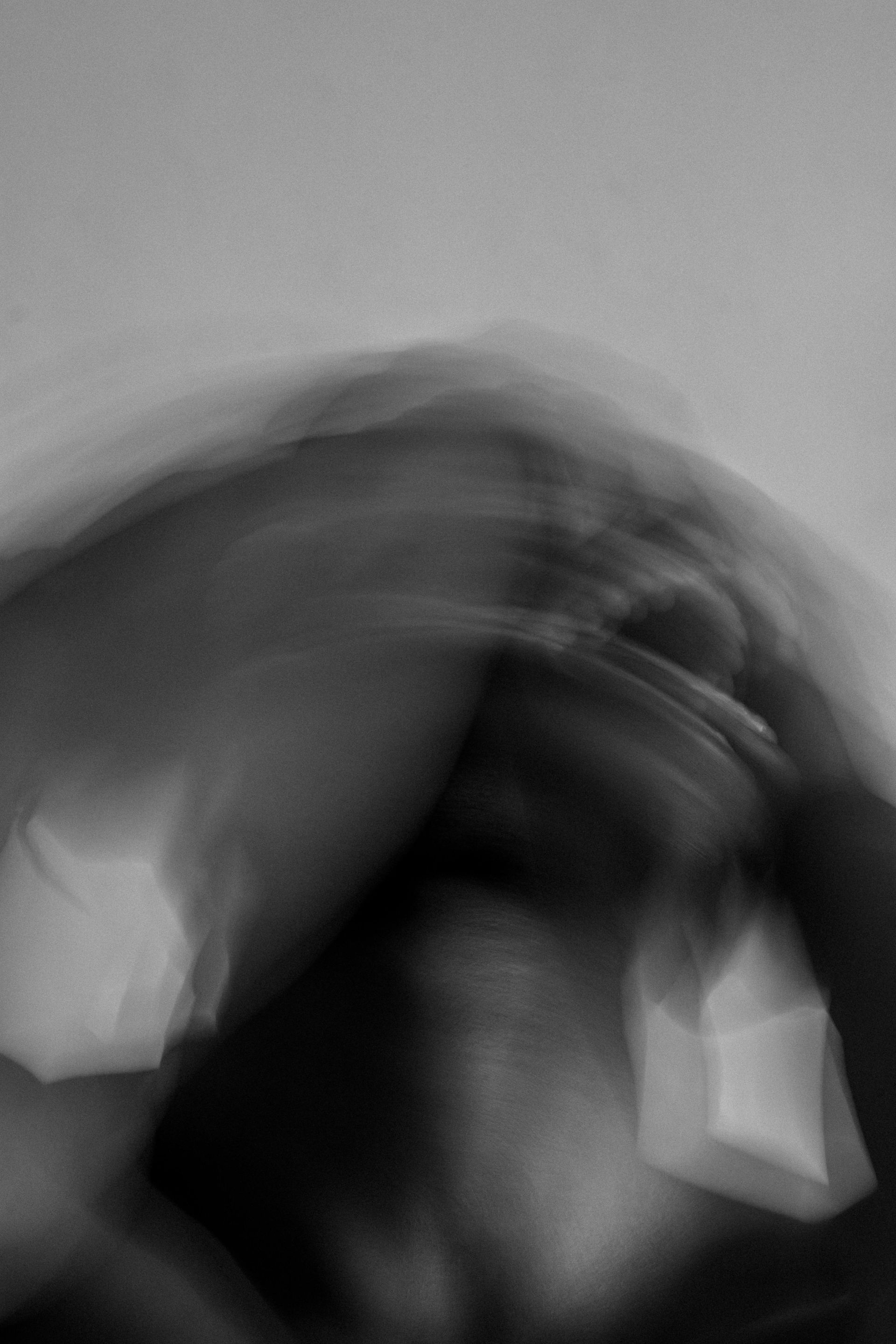 Blurred black and white photo of a person covering their head with hands, appearing distressed.