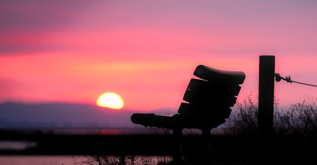 A bench is sitting in front of a sunset over a body of water.