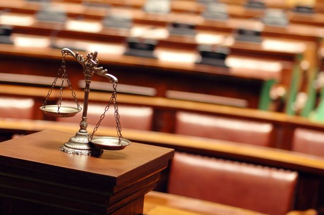 Scales of justice on a wooden stand in a courtroom with blurred wooden benches in the background.