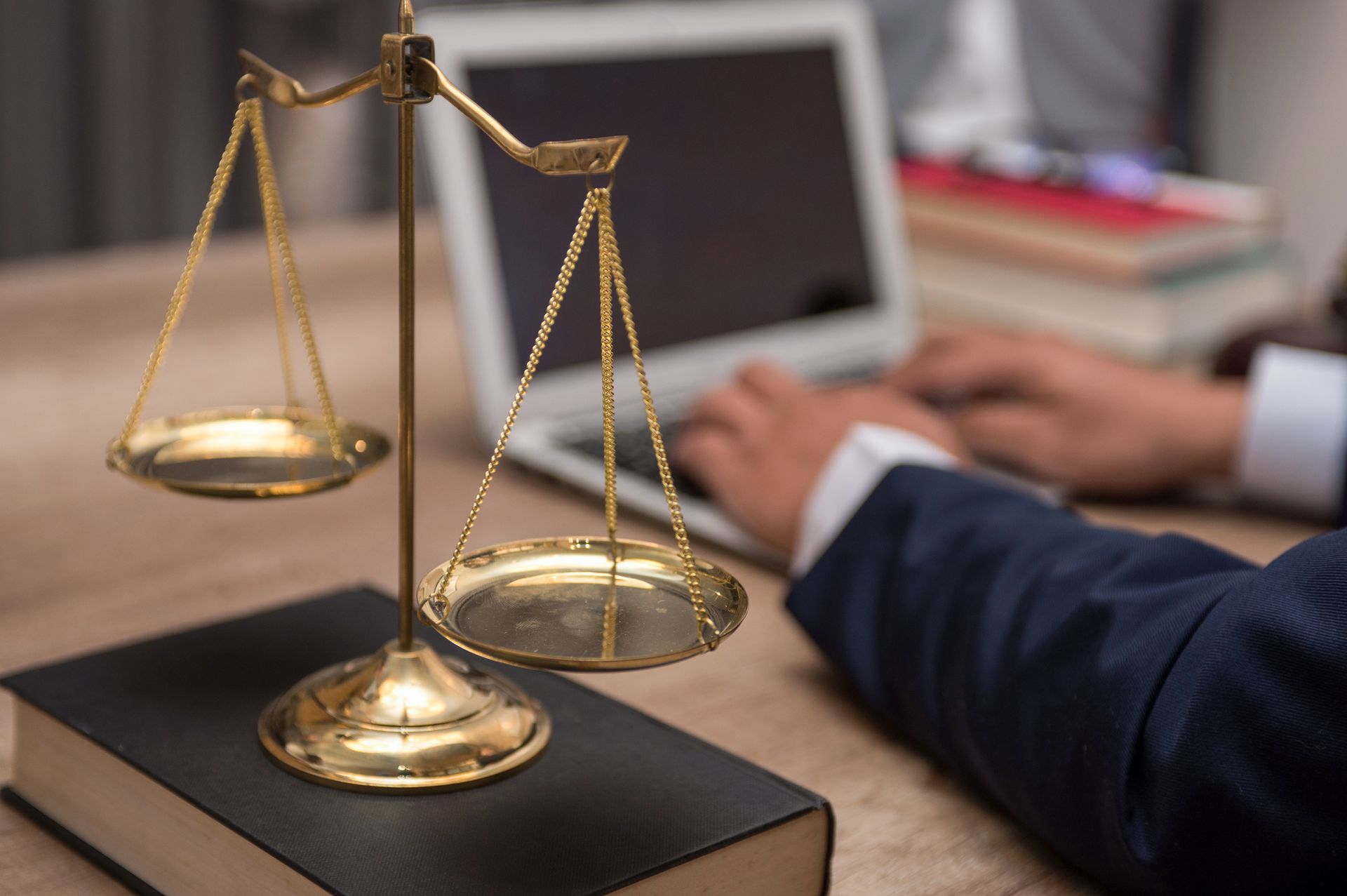 Gold scales of justice on a book, person typing on a laptop in the background.