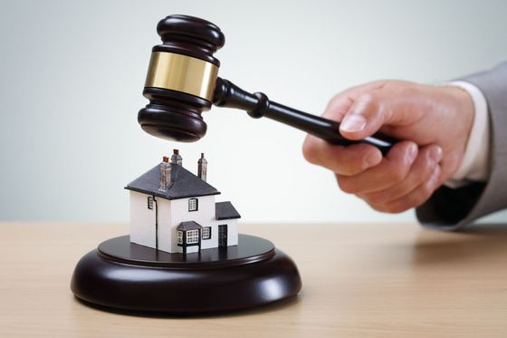 A gavel striking a miniature house on a dark wooden base, symbolizing a property auction.