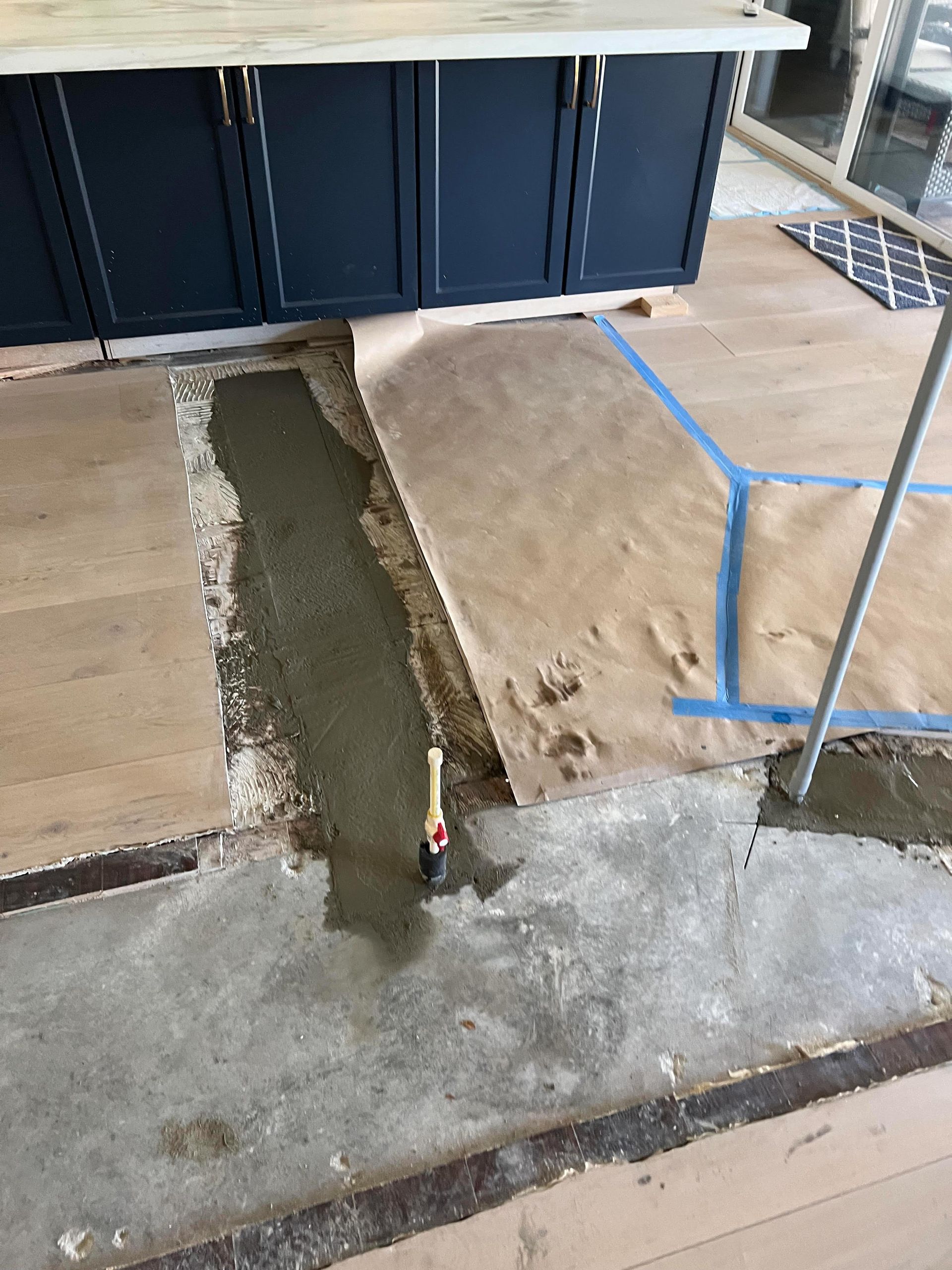 A person is laying concrete on the floor in a kitchen.