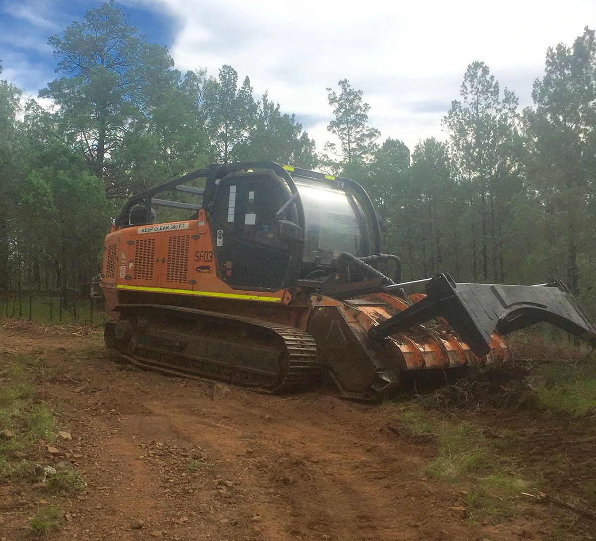 A bulldozer is driving down a dirt road in the woods.
