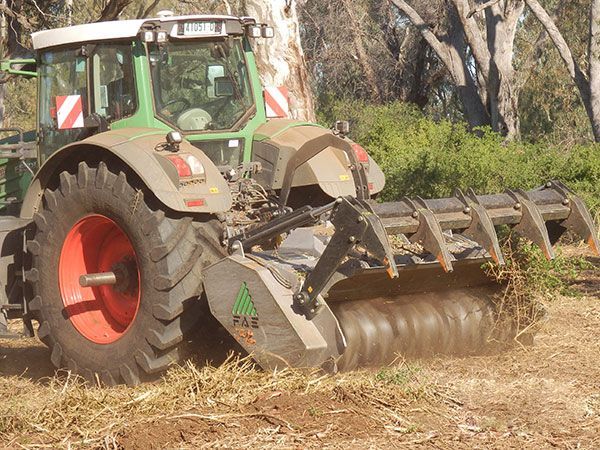A green and white tractor is plowing a field